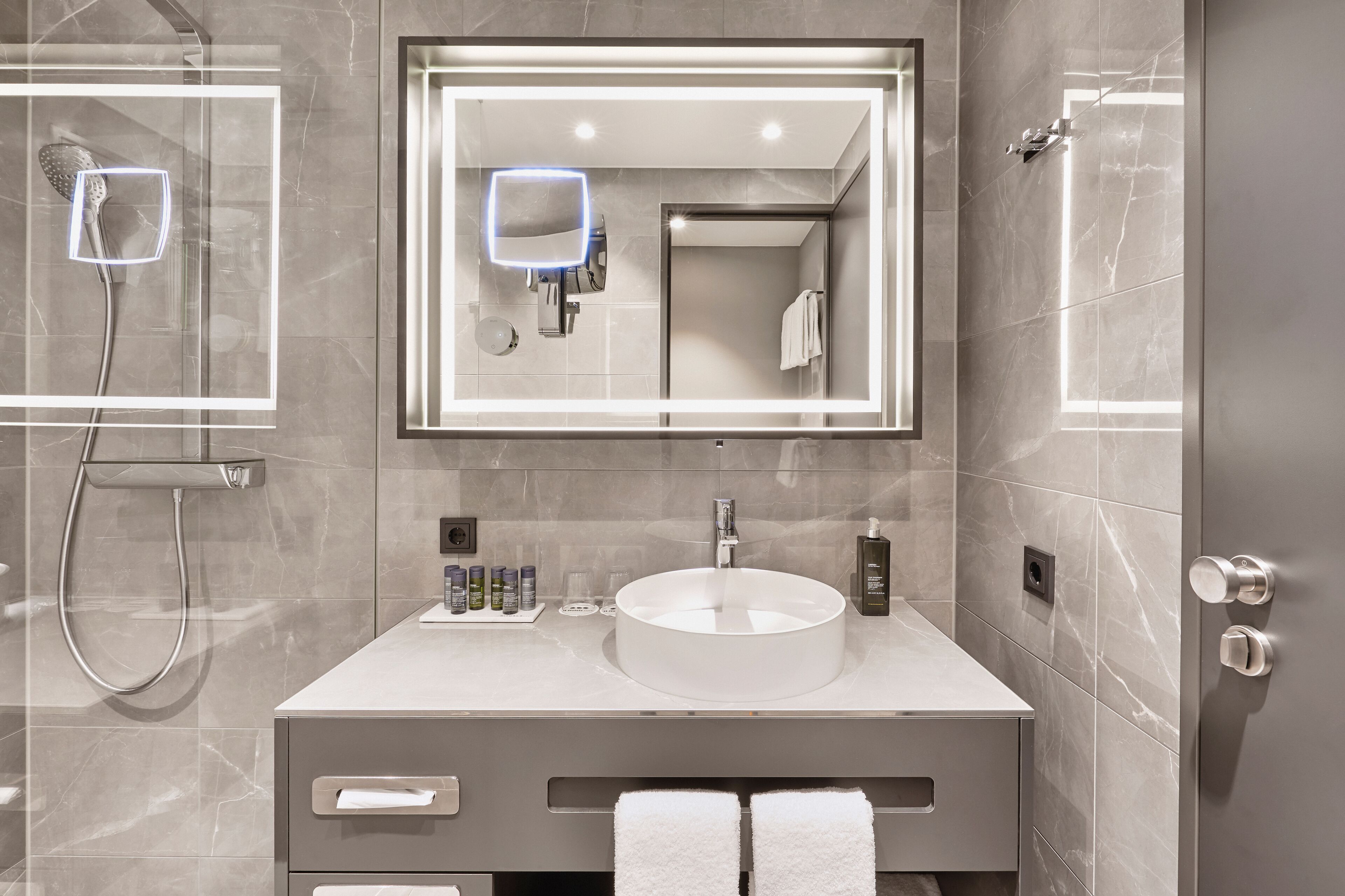 A modern bathroom with a round sink, a large mirror, and a handheld showerhead.