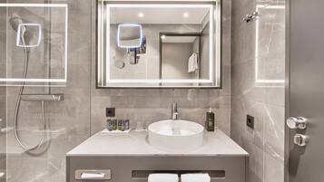 A modern bathroom with a round sink, a large mirror, and a handheld showerhead.