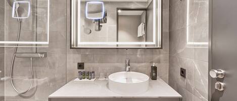 Un baño moderno con un lavabo redondo, un espejo grande y un cabezal de ducha de mano.