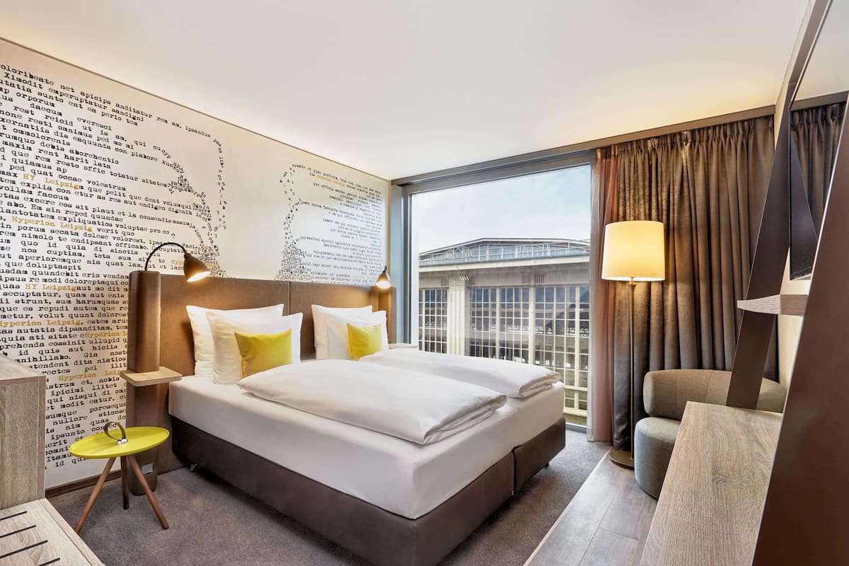 Une chambre d’hôtel moderne avec un grand lit, un bureau et une vue sur un immeuble par la fenêtre.
