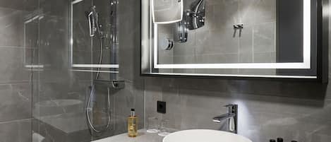 A modern bathroom with a glass shower enclosure, a large mirror, a round sink, and a vanity with a towel rack.