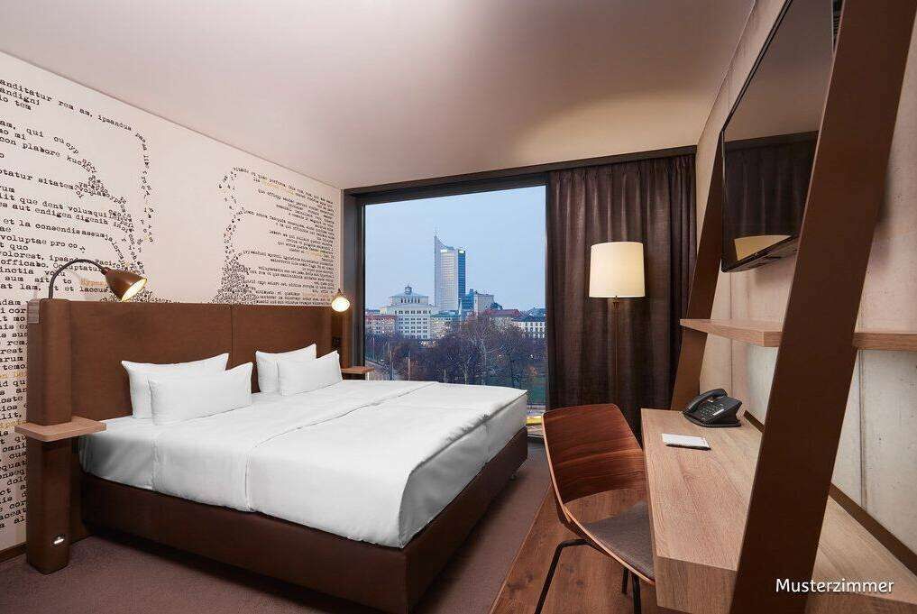 Ein Hotelzimmer mit einem großen Bett, einem Schreibtisch, einem Stuhl, einem Telefon und Blick auf eine Stadtlandschaft durch ein großes Fenster.