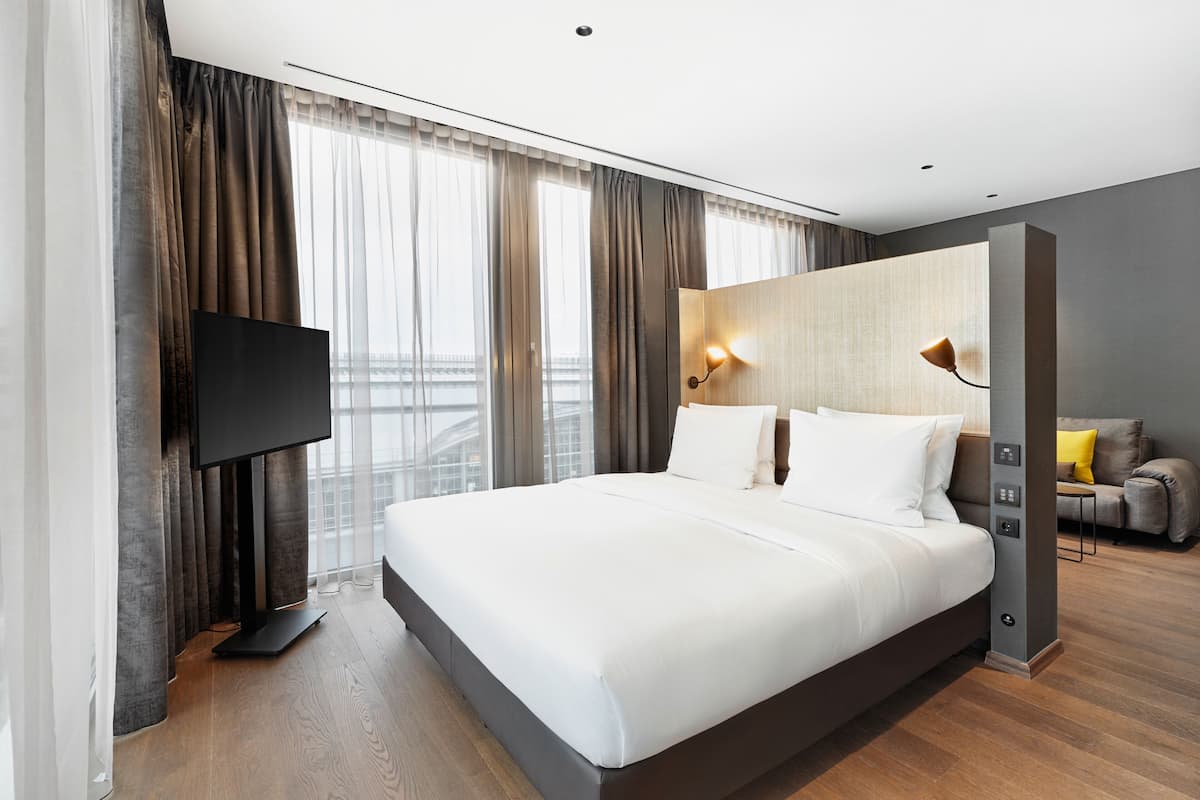 Une chambre d’hôtel moderne dotée d’un grand lit, d’une télévision à écran plat, d’un canapé et offrant une vue sur la ville.