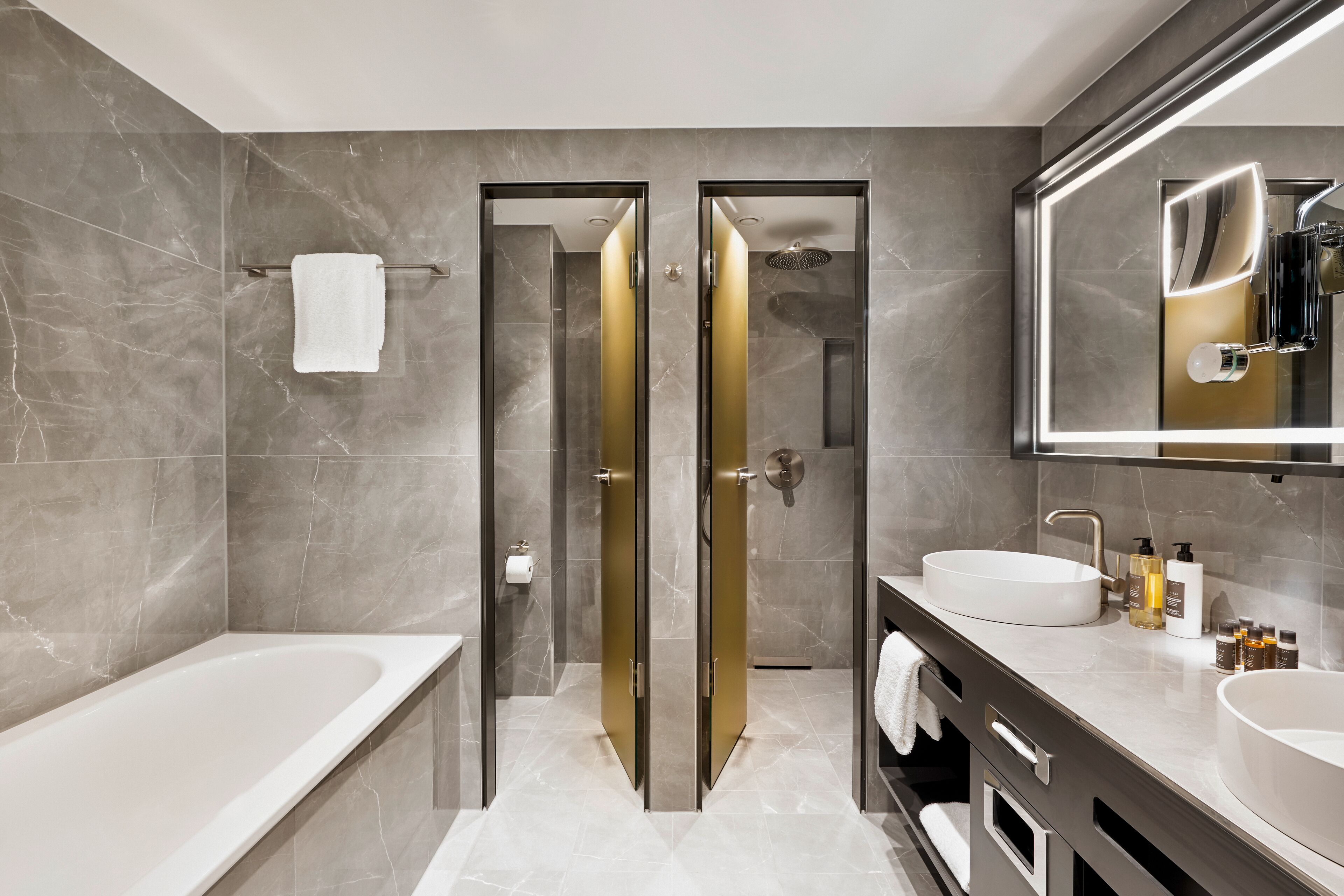 A modern bathroom with a bathtub, two vanity sinks, a large mirror, and a shower area.