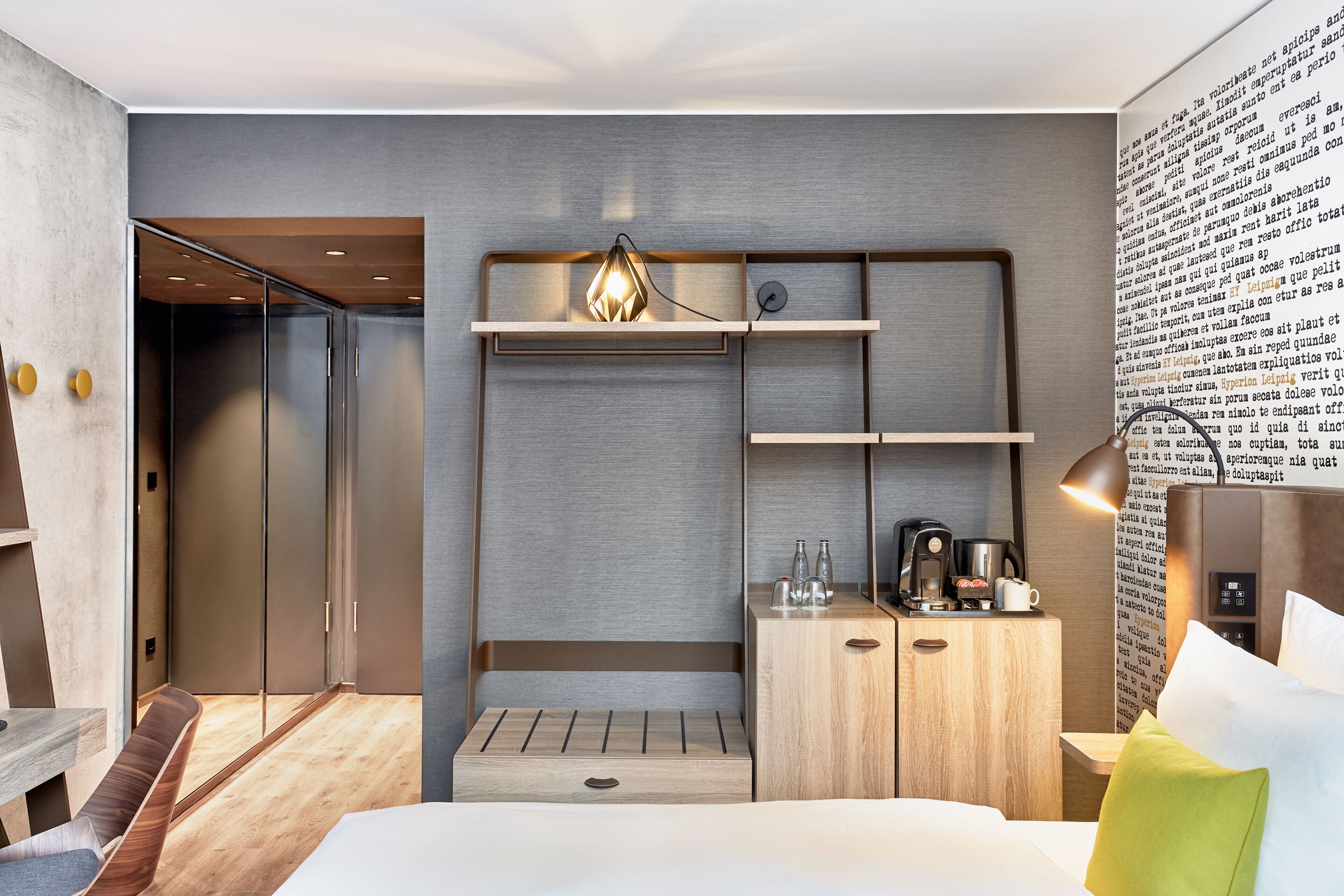 Ein modernes Hotelzimmer mit einem Bett, einer hölzernen Bank, einem Kleiderschrank und einem Schreibtisch mit Kaffeemaschine.
