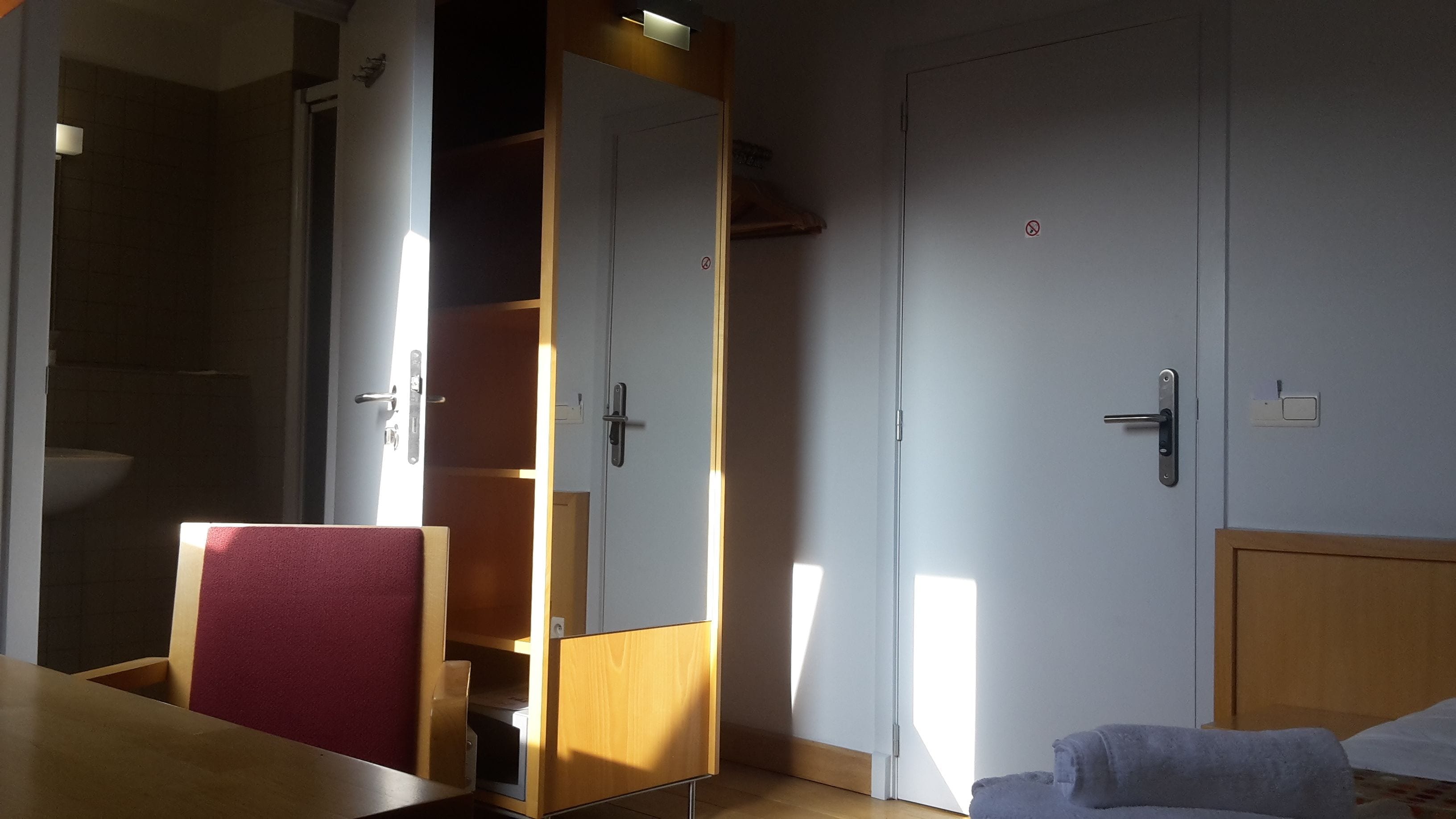 Une pièce comprenant un lit, une armoire en bois, une salle de bain avec un lavabo et une porte dotée d’une poignée.