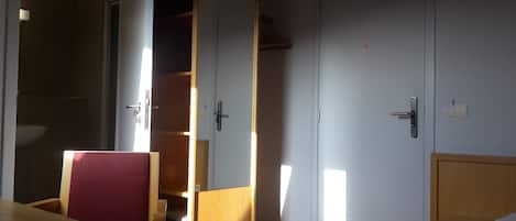 Una habitación con cama, armario de madera, baño con lavamanos y puerta con picaporte.