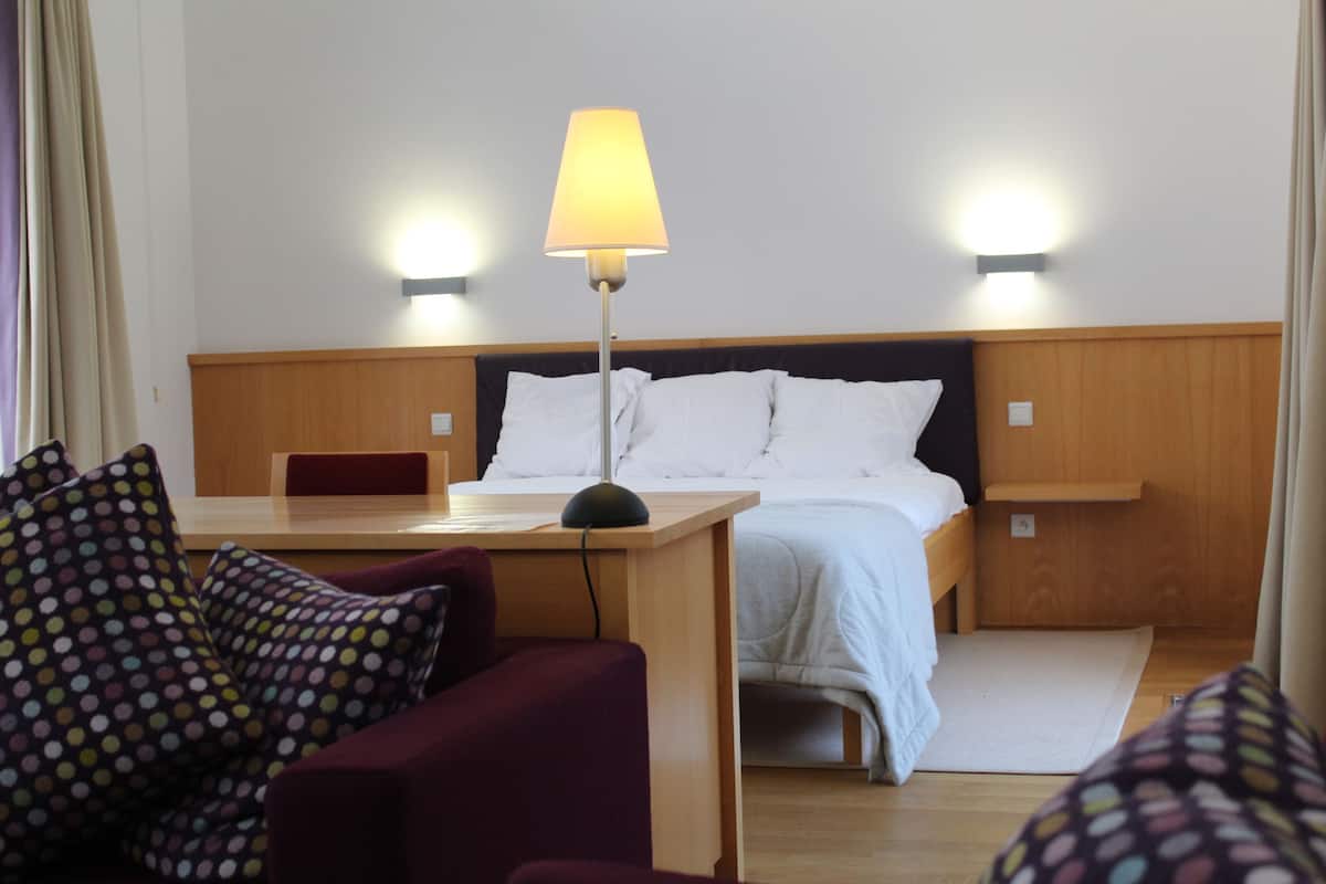 A hotel room with a bed, a desk, a chair, and a lamp.