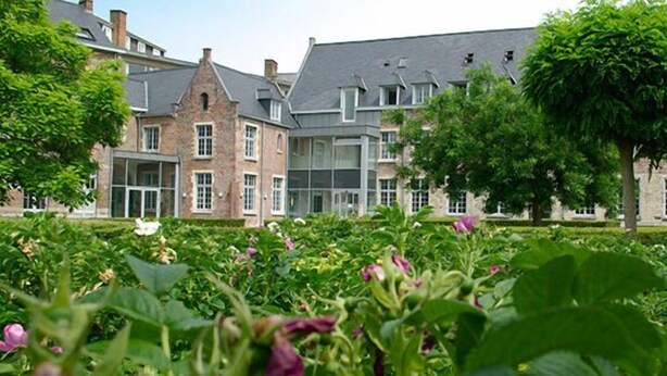 A historic building with a courtyard featuring lush greenery and flowering plants. - Irish College Leuven (Leuven)