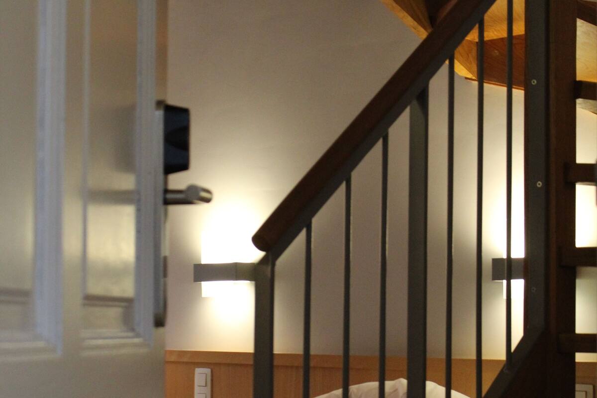 A staircase leading to a bedroom with a bed, a nightstand, and a wall-mounted lamp.
