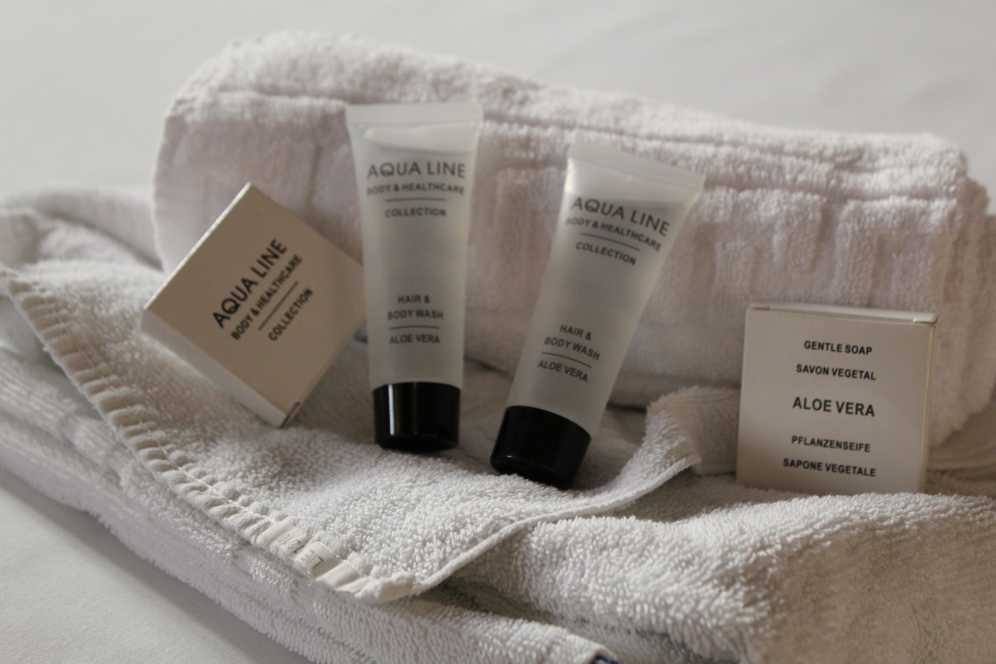 Una toalla blanca con tres botellas de jabón corporal Aqua Line y una caja de jabón Gentle Soap.