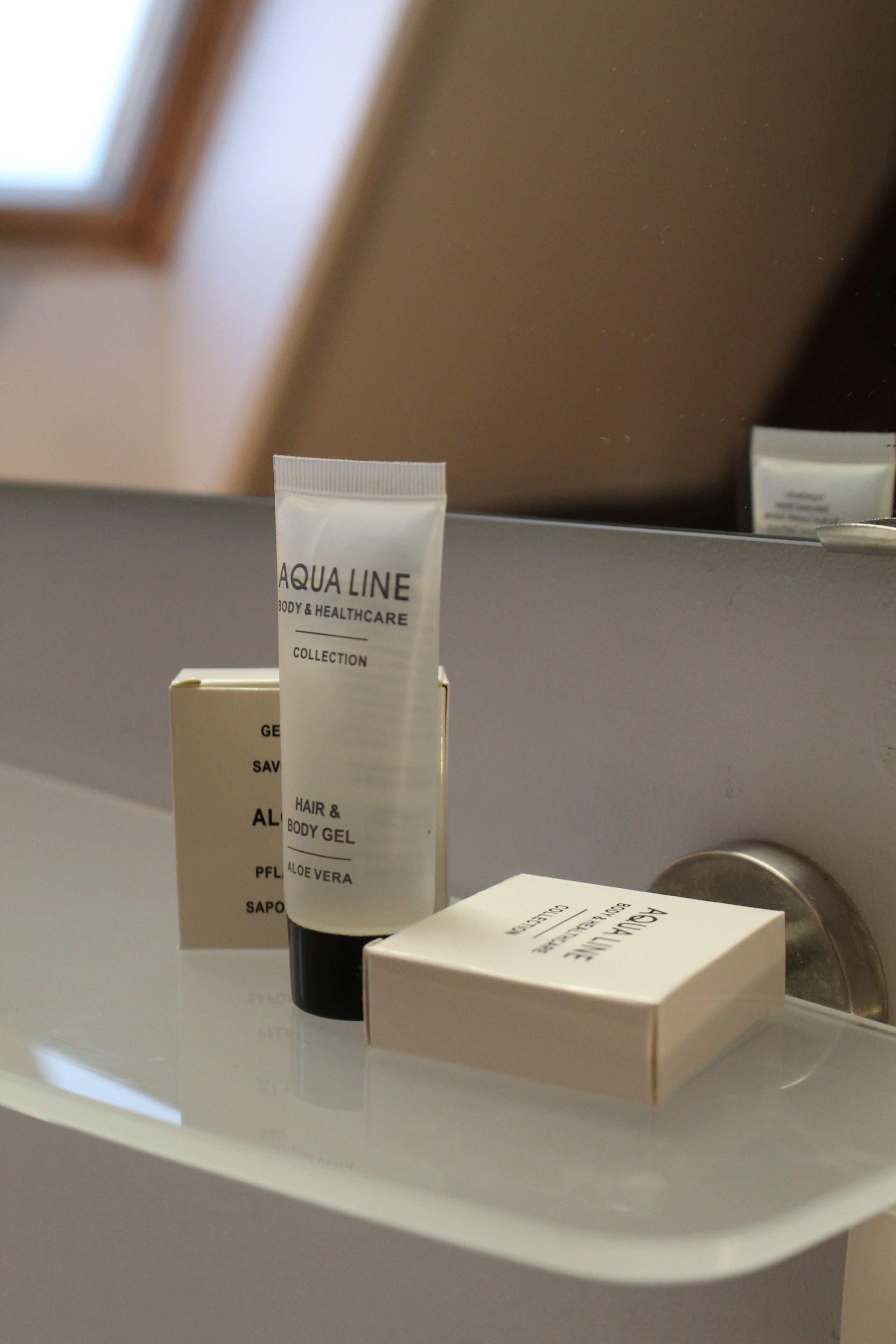Ett tubformat schampo och duschgel från Aqua Lines serie för kroppsvård och hygien, placerat på en vit yta tillsammans med en kartong märkt med "Aqua Line" och en annan kartong med text.