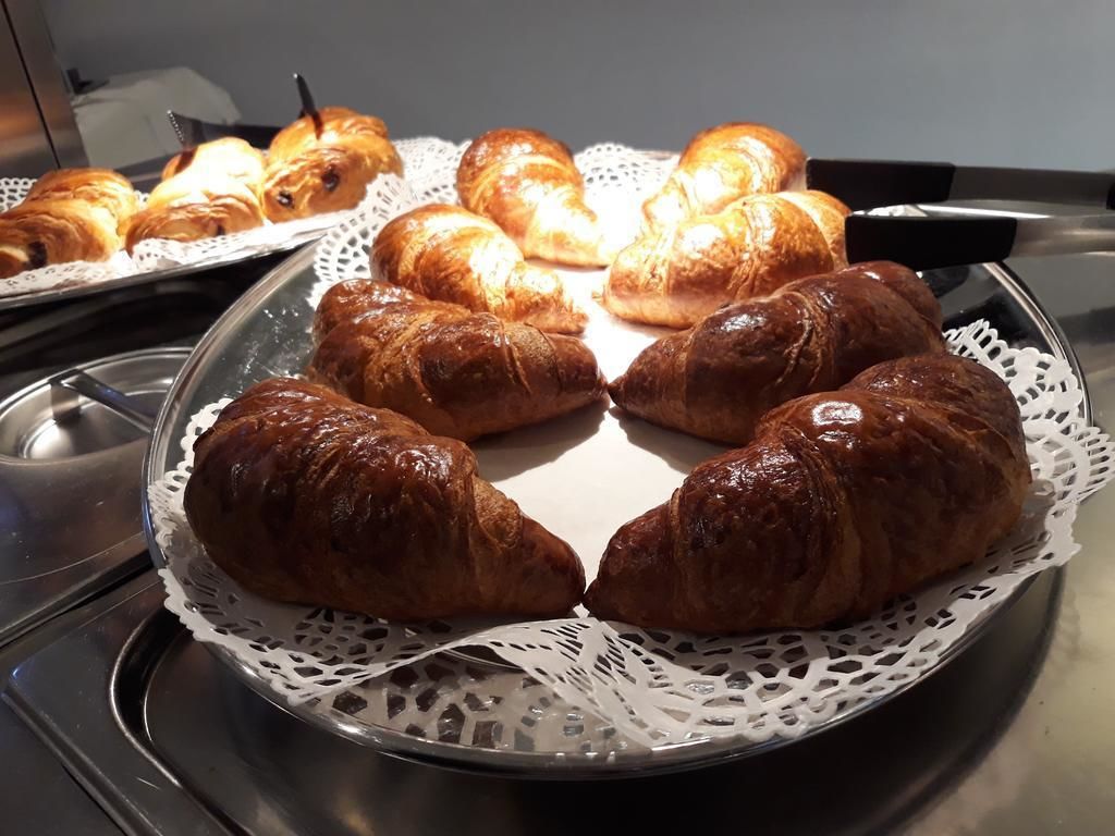 Una bandeja con diversos pasteles, incluyendo croissants y otras delicias horneadas, dispuesta sobre una bandeja de metal con un mantel de encaje blanco.