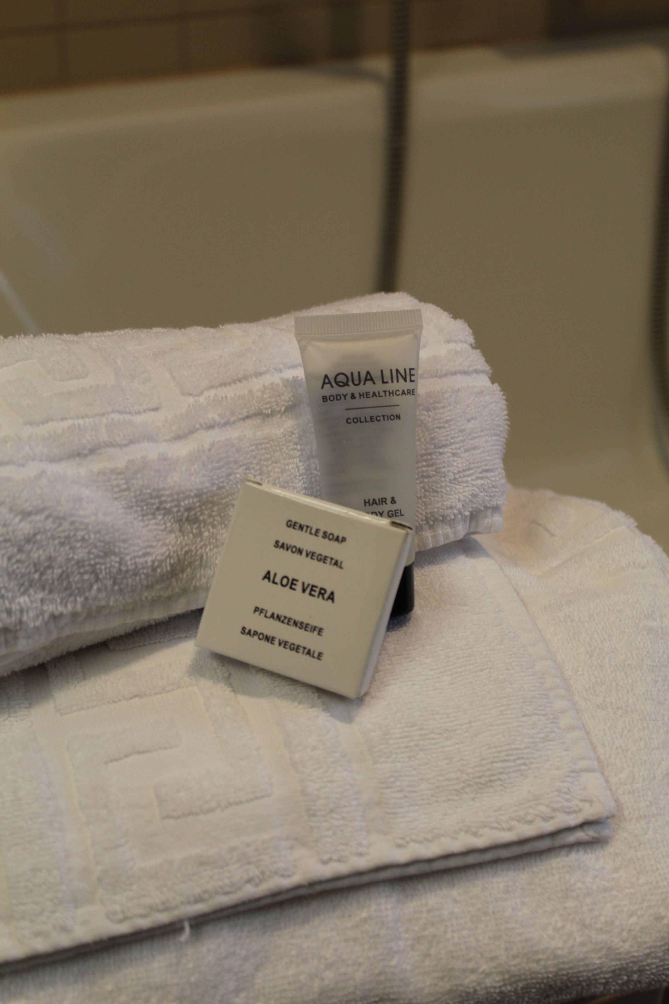 A bathroom with a white towel and a bottle of Aqua Line body and healthcare collection.