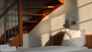 A bedroom with a wooden staircase, a bed with white bedding, and a wall-mounted light fixture. - Irish College Leuven (Leuven)