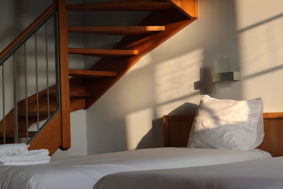A bedroom with a wooden staircase, a bed with white bedding, and a wall-mounted light fixture.