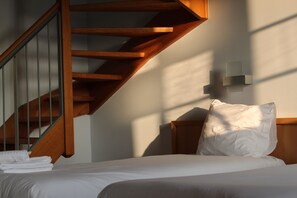 A bedroom with a wooden staircase, a bed with white bedding, and a wall-mounted light fixture. - Irish College Leuven (Leuven)
