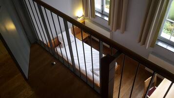 Un dormitorio con piso de madera, una cama con ropa blanca, una mesita de noche y una ventana con cortinas.