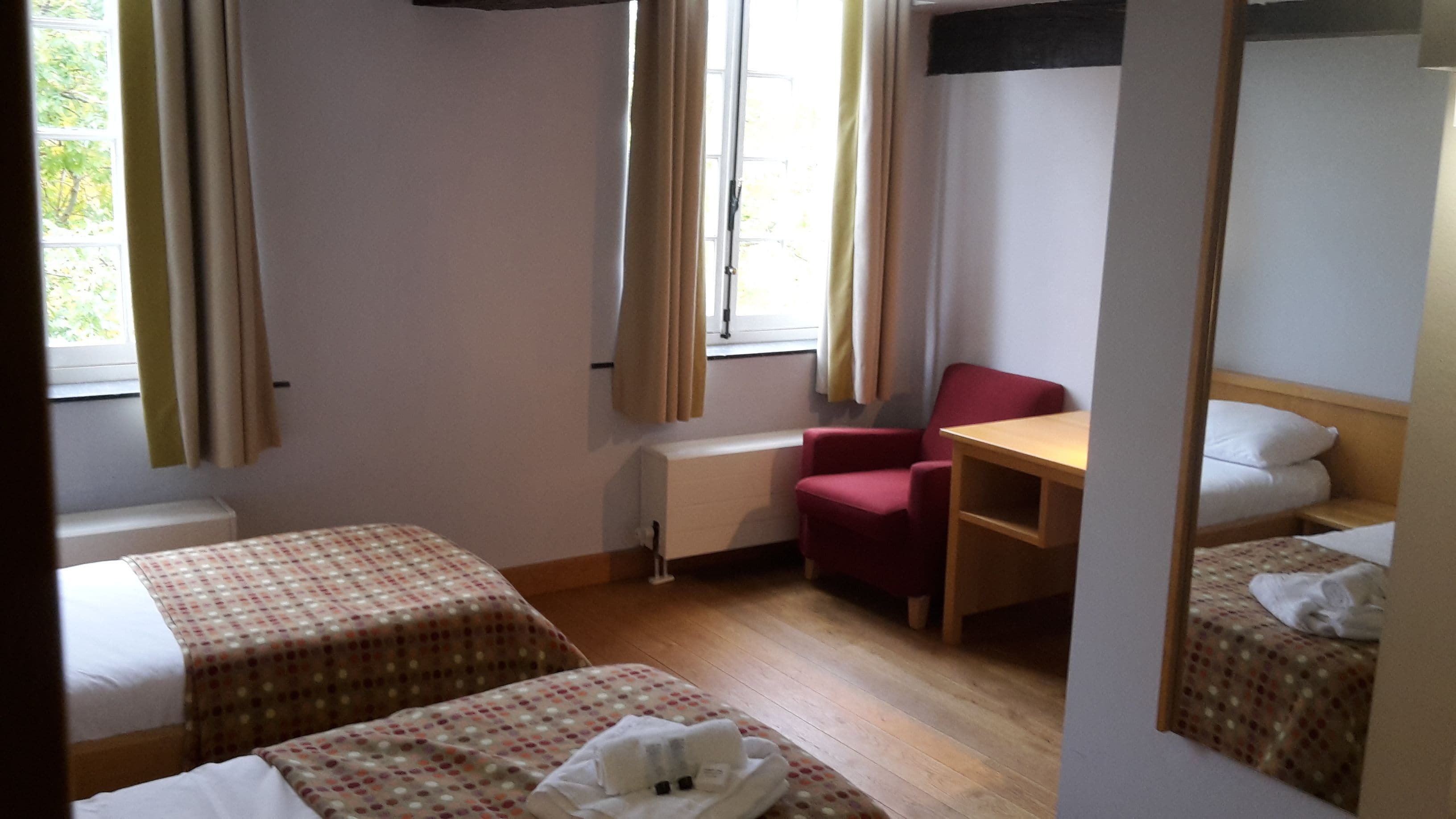 Una habitación de hotel con dos camas, un escritorio, una silla y una ventana con cortinas.