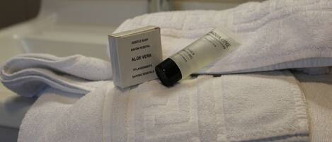 Une salle de bain avec une serviette blanche, un flacon de savon à l’aloe vera et une boîte du même produit.