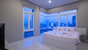 A modern bedroom with a large bed, a TV, and a city view through large windows. - SSB Residence (Phnom Penh)