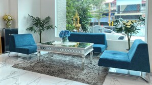 A modern living room with a large window, a blue sofa set, a glass coffee table with a vase of flowers, and a decorative plant. - SSB Residence (Phnom Penh)