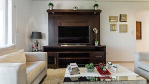 A living room with a dark wood entertainment center, a flat-screen TV, a white sofa, a coffee table with books and decorative items, and framed pictures on the wall. - Trendy Barrio Jara apartment (Asunción)