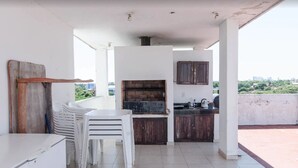 A kitchen with a built-in grill, white cabinets, and a dining area with stacked chairs. - Trendy Barrio Jara apartment (Asunción)