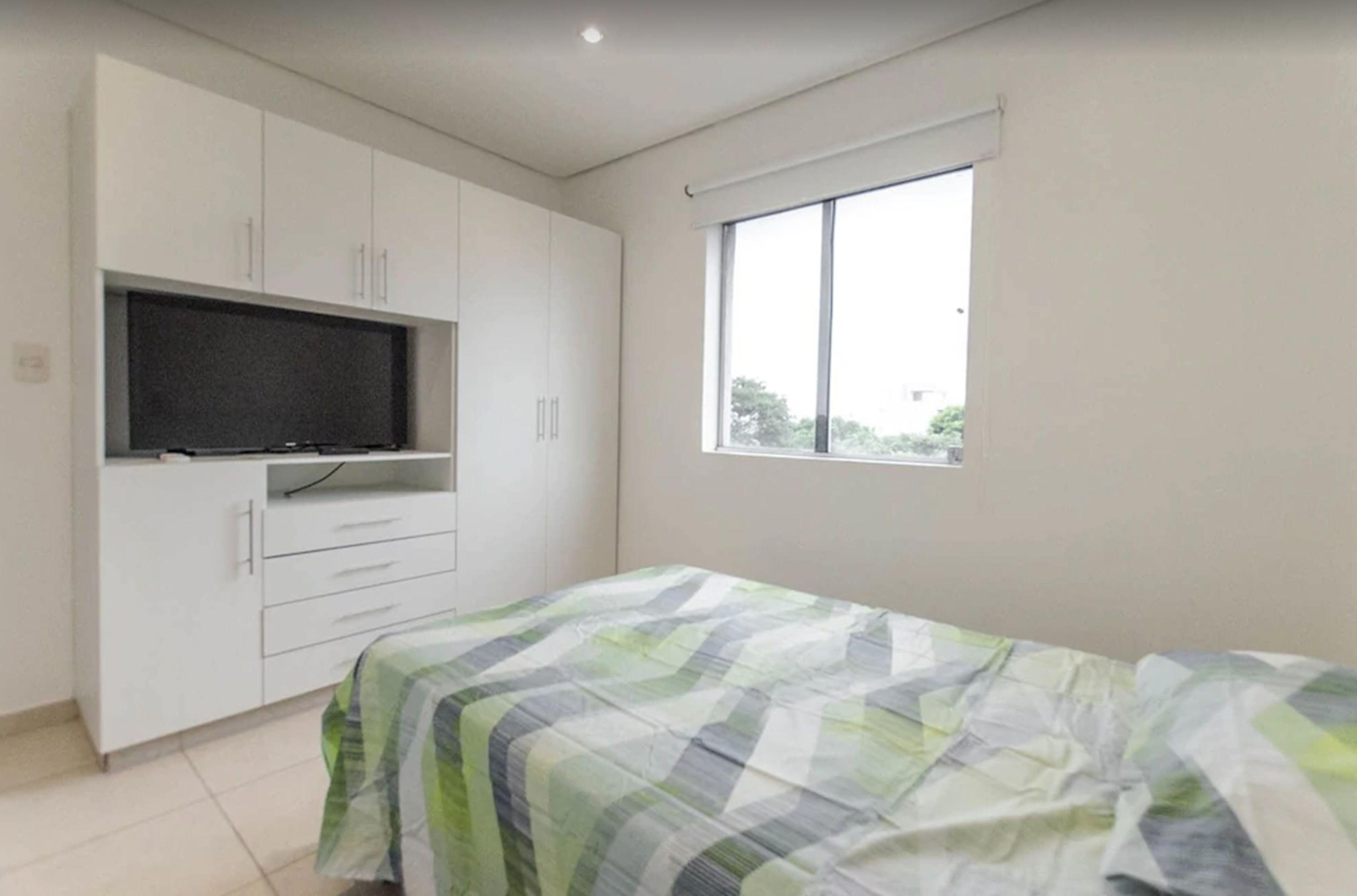 A bedroom with a bed, a TV mounted on a cabinet, and a window with a view of trees.