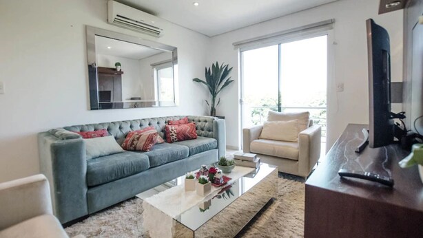 A modern living room with a grey sofa, a beige armchair, a glass coffee table, and a large mirror on the wall. - Trendy Barrio Jara apartment (Asunción)