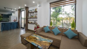A modern living room with a sofa, a coffee table, and a kitchen area with a refrigerator and bar stools. - Lena Homestay (Da Nang)