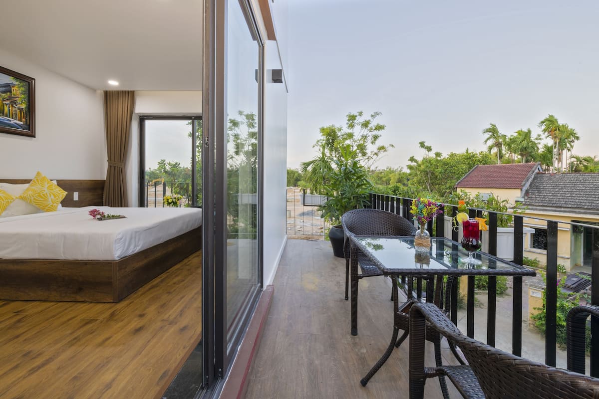 A hotel room with a balcony, a bed, a table with chairs, and a view of the surrounding area.