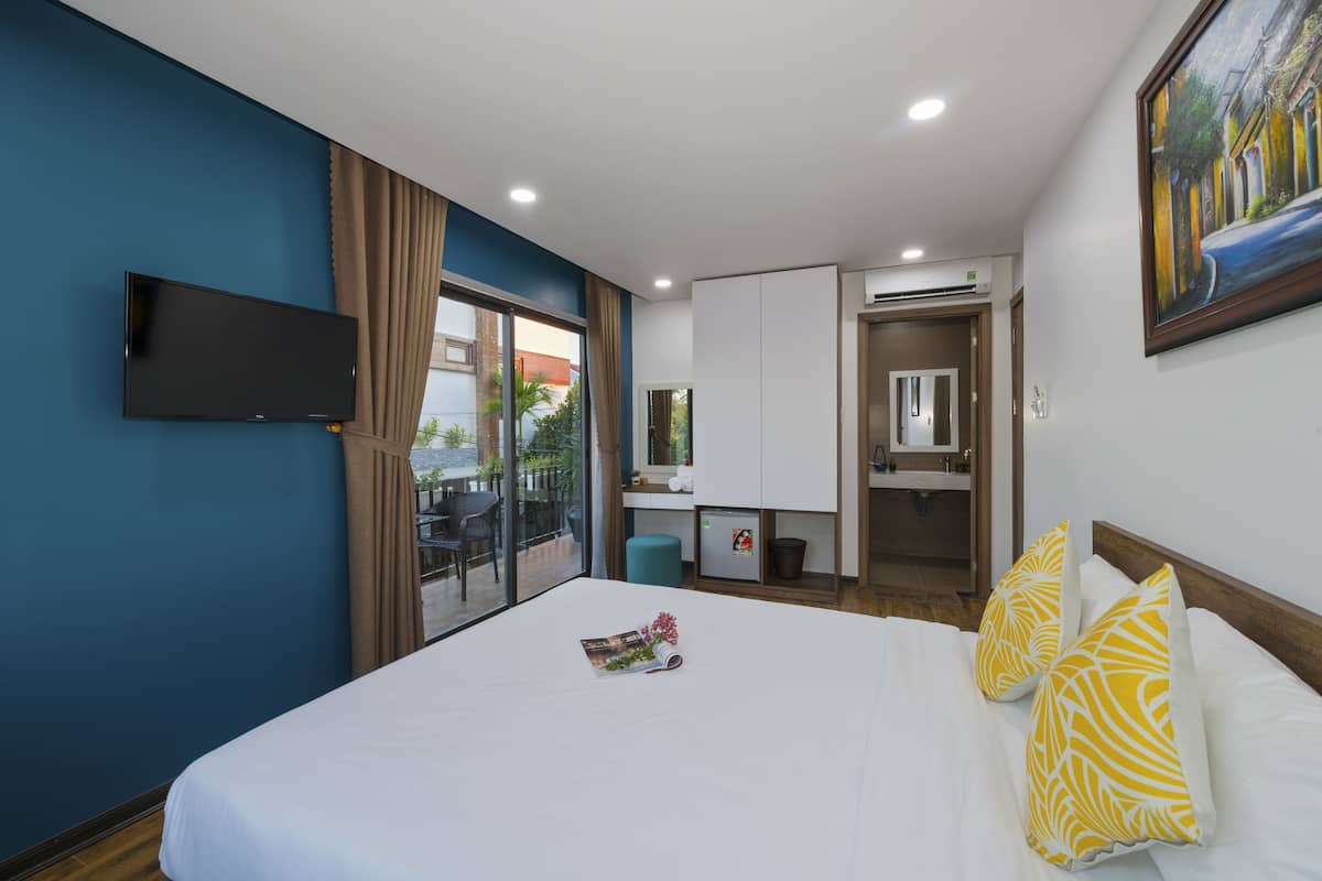 A hotel room with a large bed, a flat-screen TV mounted on the wall, a small kitchenette, and a sliding glass door leading to an outdoor area.
