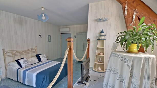 Un dormitorio con cama, un escritorio con una planta, un estante pequeño con adornos y un ventilador de techo.