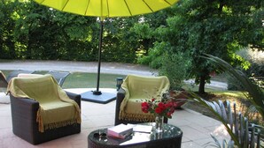 Un patio al aire libre con mobiliario de mimbre, un paraguas amarillo y un jarrón con flores rojas.