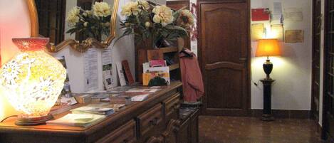 A reception area with a wooden desk, a large mirror, a vase with flowers, a lamp, and a door.