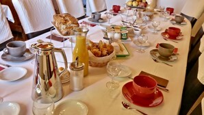 Desayuno preparado para cuatro personas, con croissants, fruta, café y copas de vino.