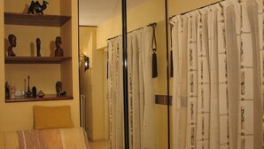 Una habitación con cama, un espejo, estantes con adornos y una cortina de ducha estampada.