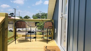 Une terrasse en bois avec deux chaises en métal et un paillasson sur lequel est écrit le mot « bonjour ».