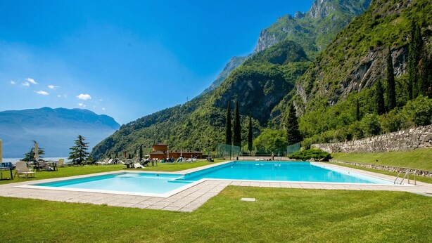 A swimming pool with a mountain backdrop, surrounded by a grassy area and a stone wall. - Casa Turchese with Private Garden, Pool and Tennis, Riva del Garda, Italy (Riva del Garda)