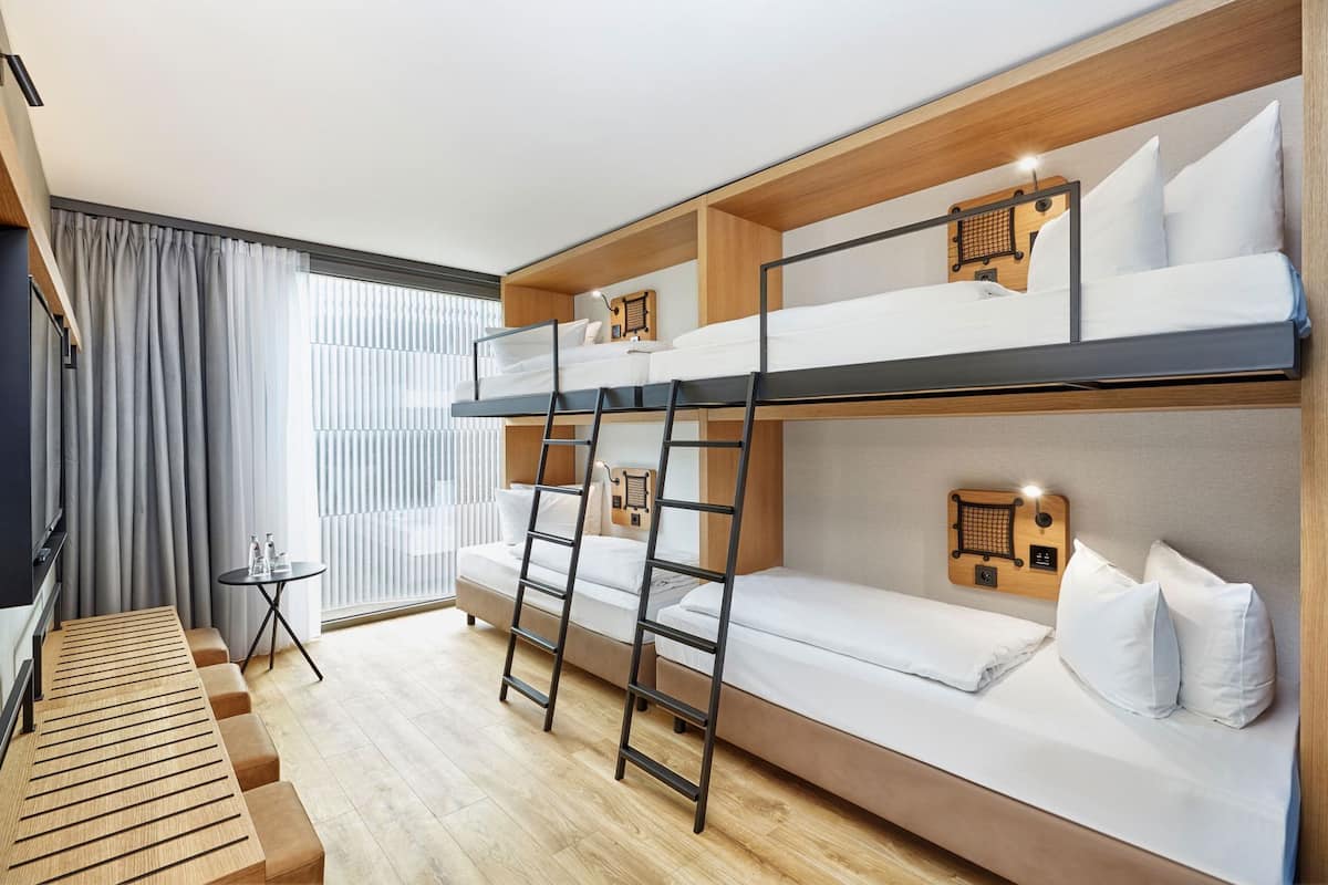 A bunk bed room with a wooden ladder, a small table with bottles, and a bench.