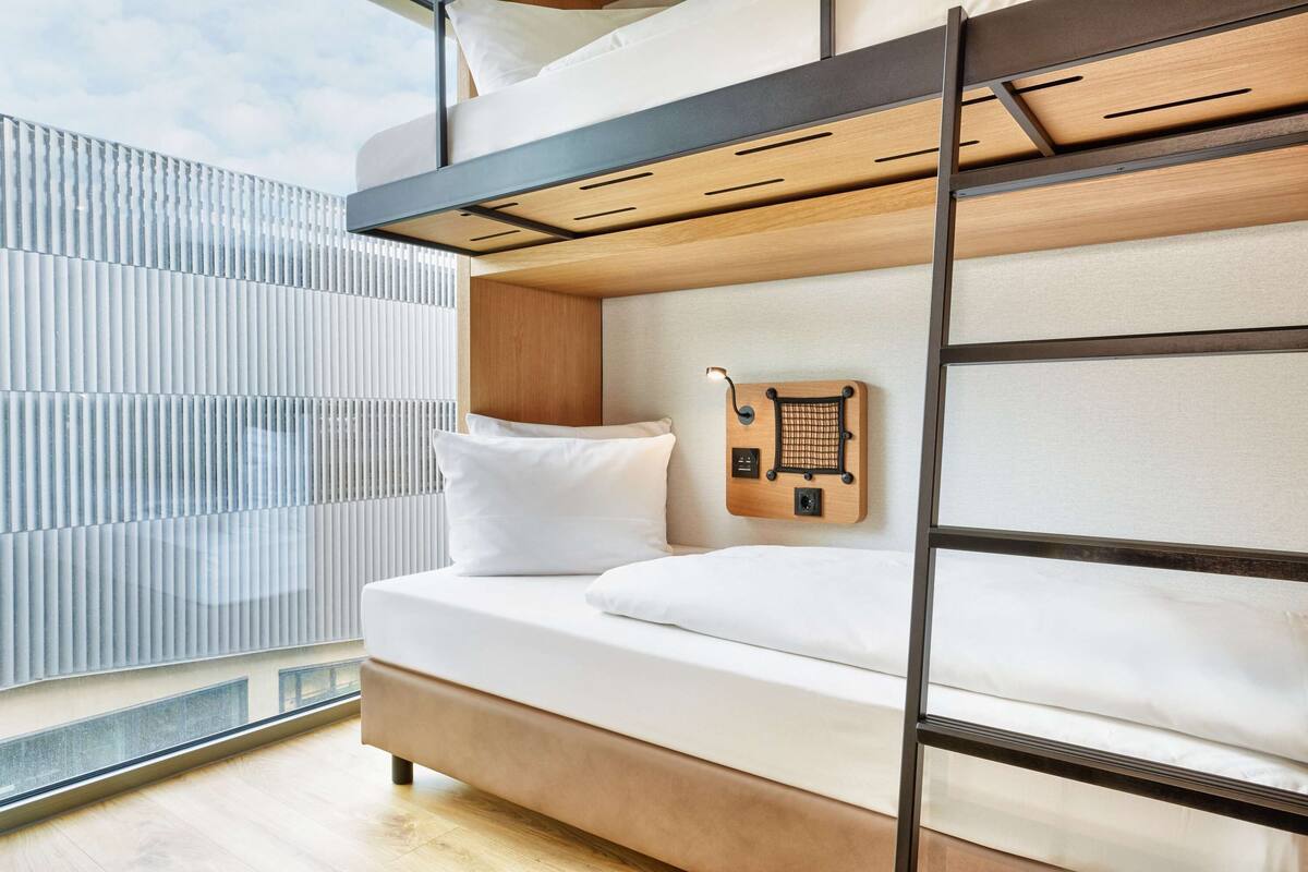 A bunk bed with a wooden ladder, white bedding, and a small wooden shelf with a hook.