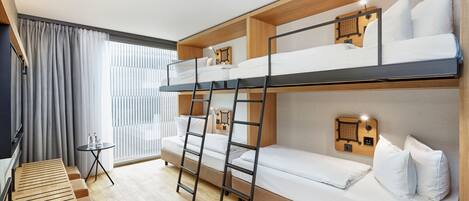 Habitación con literas, una escalera de madera, una mesita con botellas y una ventana con cortinas.
