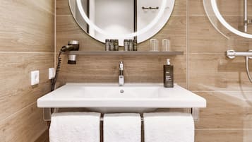 Un baño con un lavamanos blanco, dos toallas blancas, un espejo redondo con luces y una zona de ducha.
