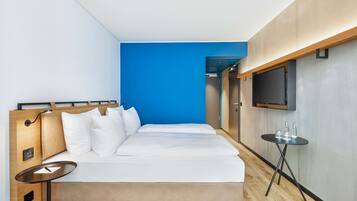 Una camera d'albergo moderna con un letto grande, un tavolino, una TV e una parete decorata in blu.