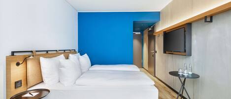 Una habitación de hotel moderna con una cama grande, una mesita pequeña, un televisor y una pared azul decorativa.