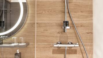 Un baño moderno con ducha, espejo con luz y repisa con artículos de aseo.