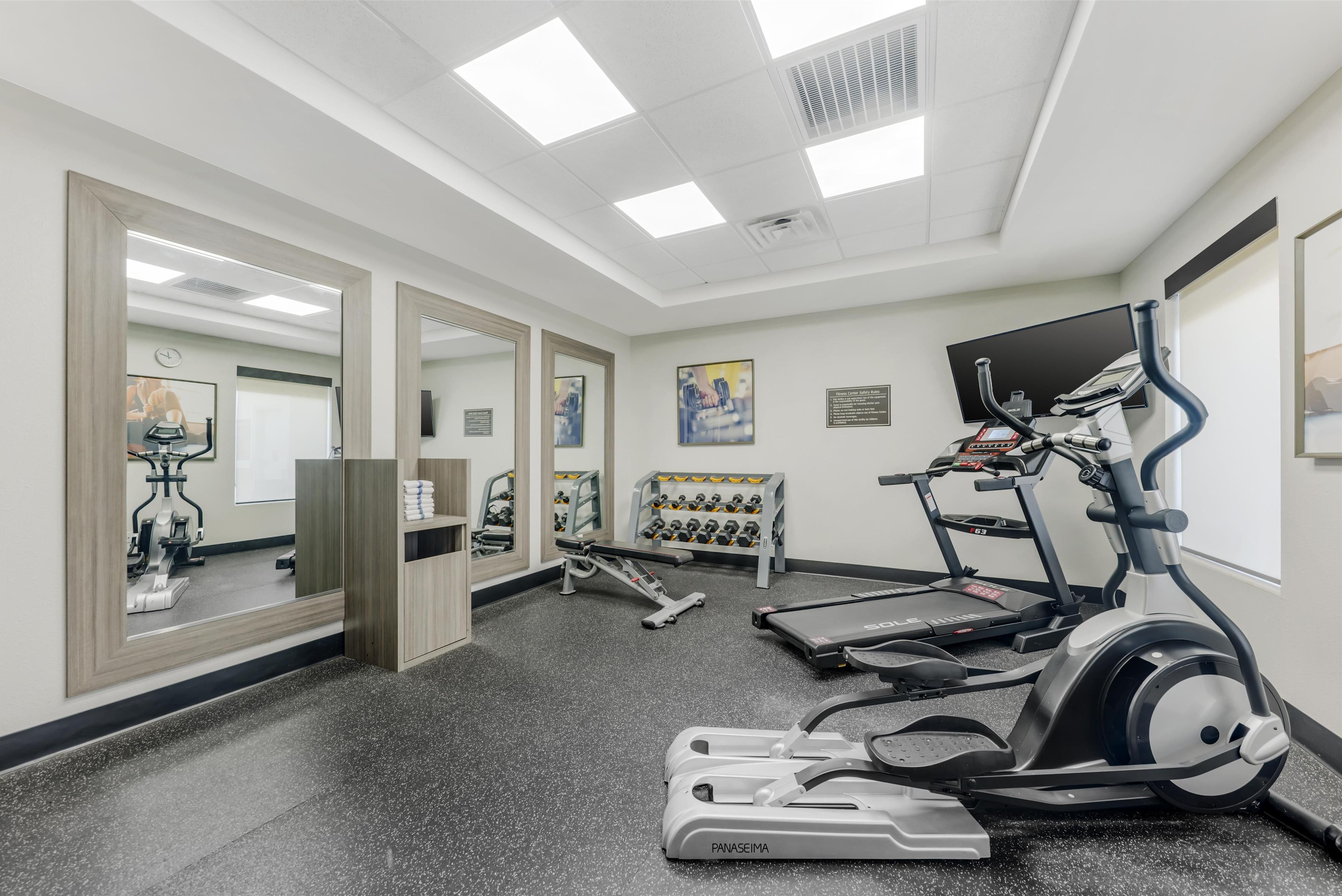 Ein Fitnessraum mit Laufbändern, Crosstrainern und einer Gewichtbank.