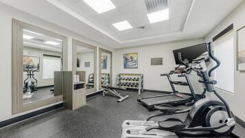 Ein Fitnessraum mit Laufbändern, Crosstrainern und einer Gewichtbank.