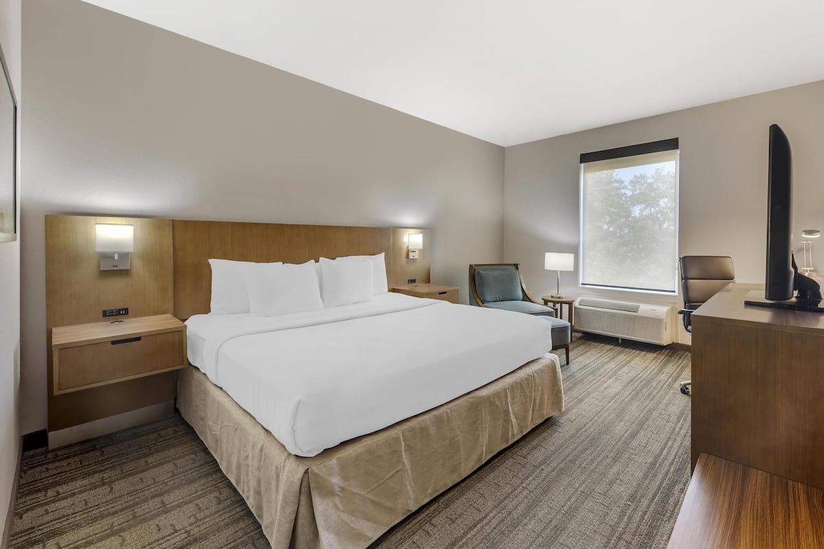 Hotellihuone, jossa on suuri sänky, yöpöydät, työpöytä, tuoli, ikkuna ja työpöytälamppu.